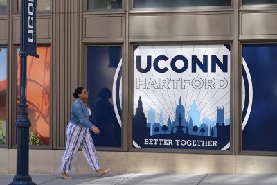 A student walks outside of the Hartford Times Building pas a sign that reads UConn Hartford: Better Together.