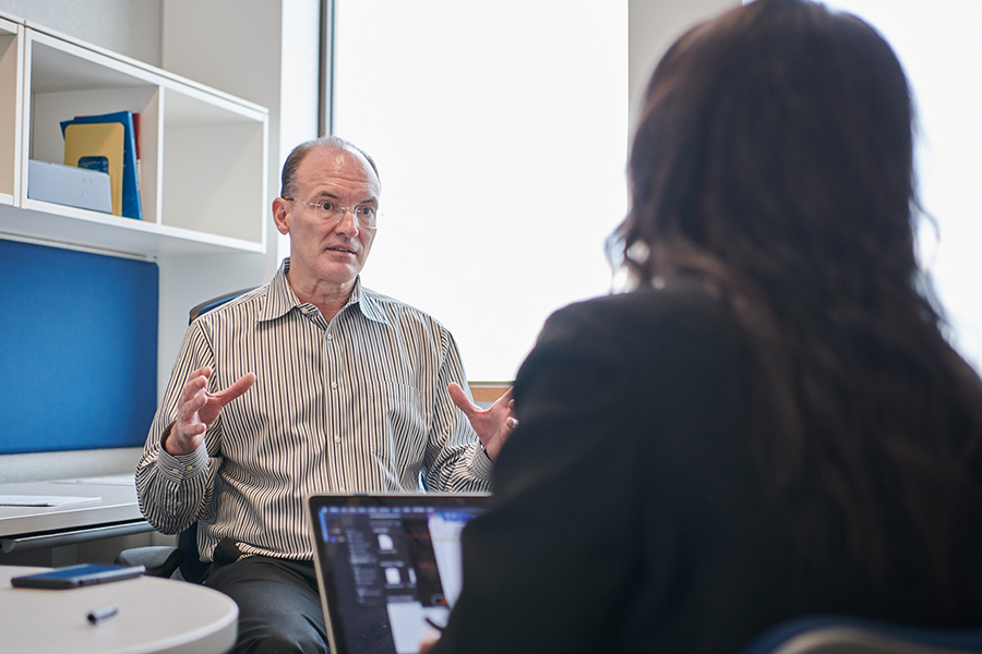 A professor gestures while talking with a student in his office. 