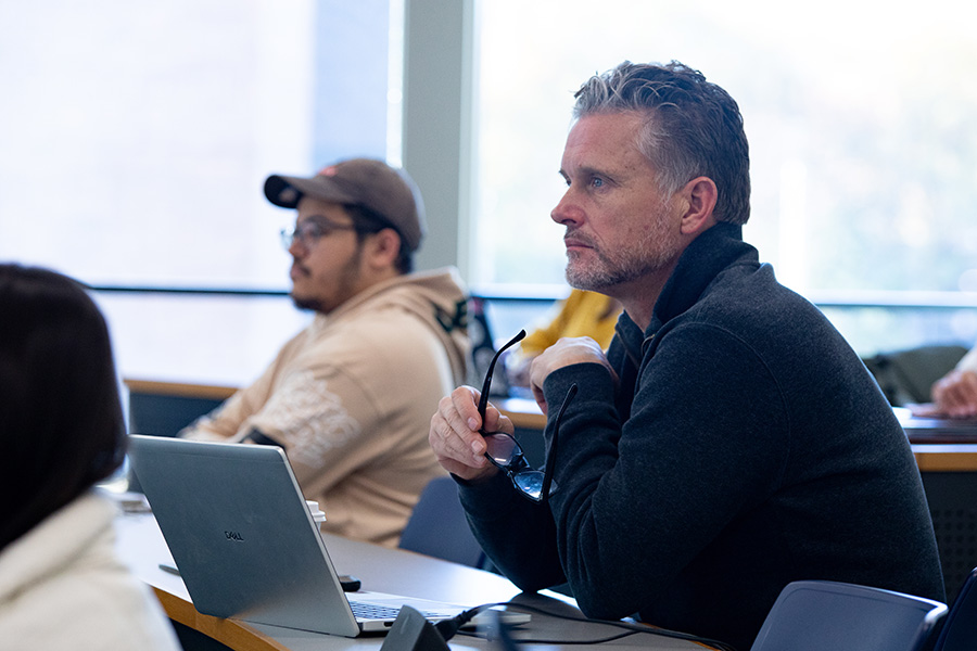 A seminar class with two people listening to a lecture in front of laptops.